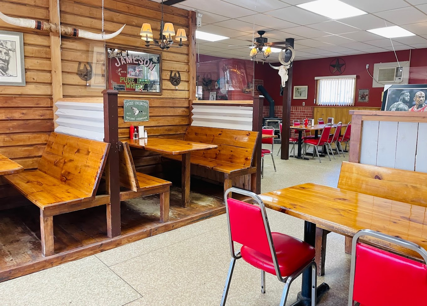 A restaurant dining room with wooden walls and tables, red chairs, and western decor 