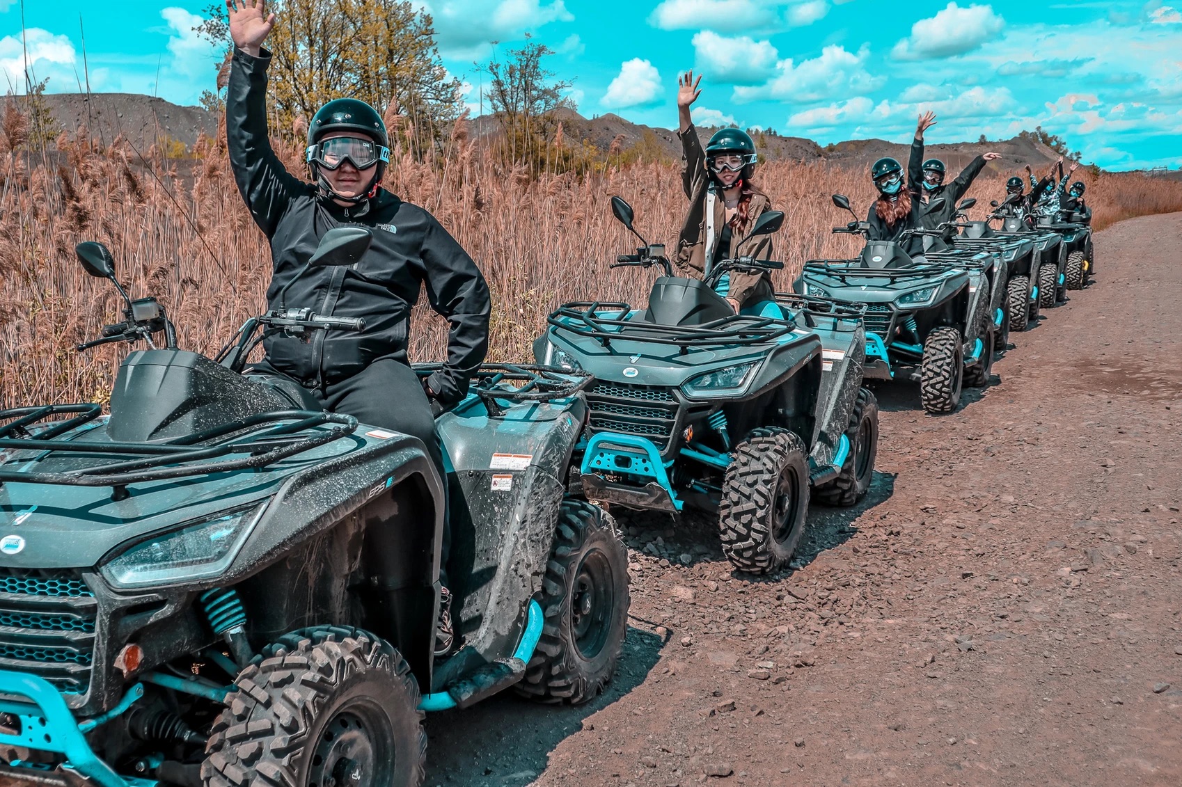 Multiple ATVs with people on them waving to the camera 