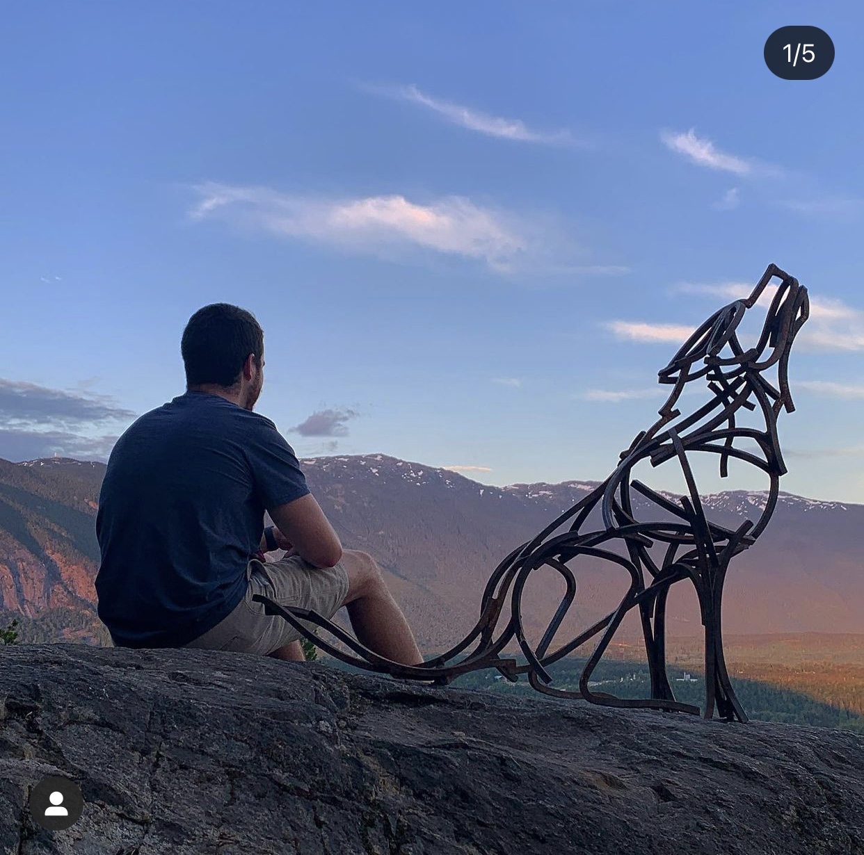 hiker sitting next to metal wolf sculpture at lookout