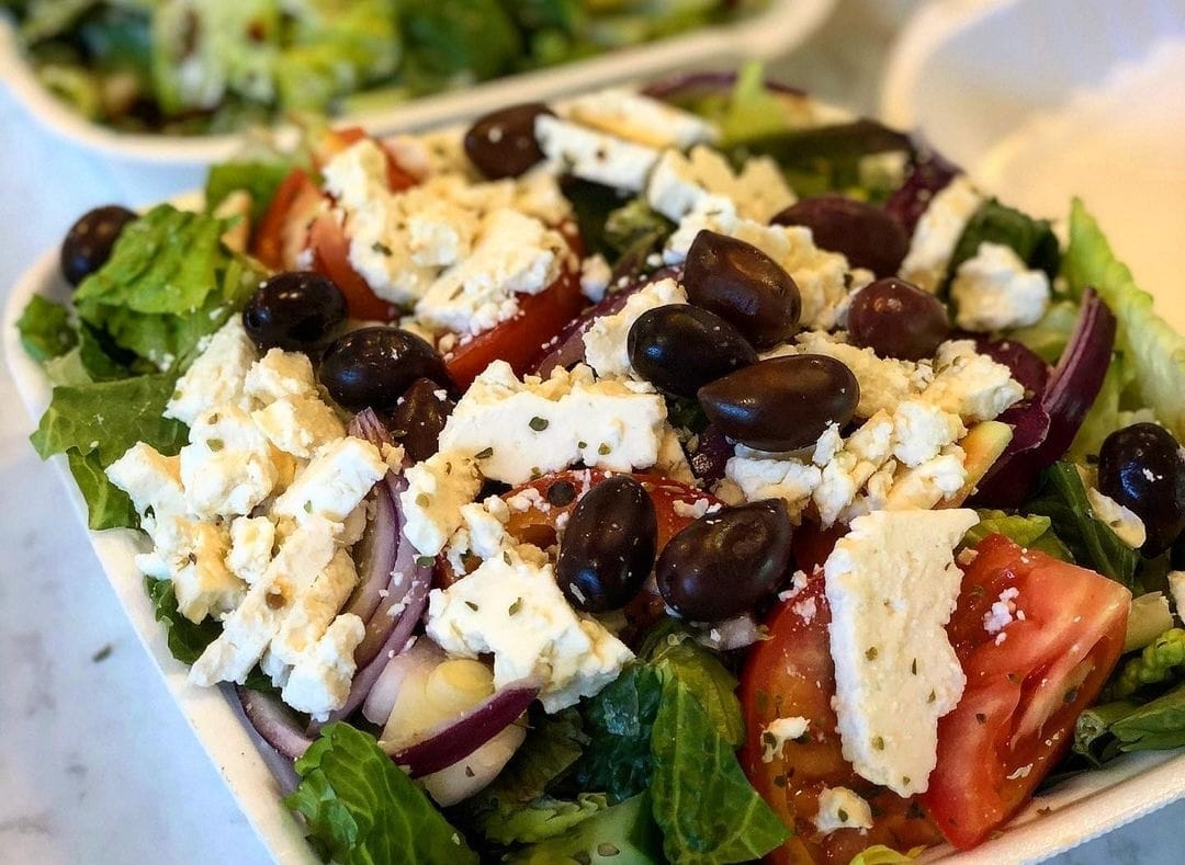 a close up of a bowl of salad with cheese and olives on top