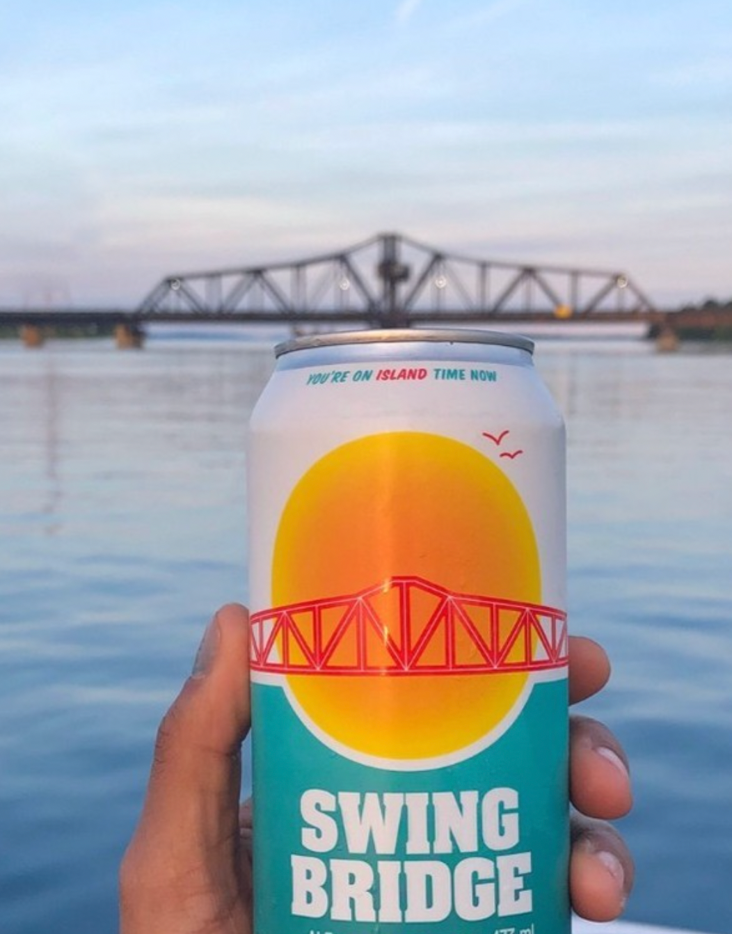 a can of beer with a lake and a bridge in the background