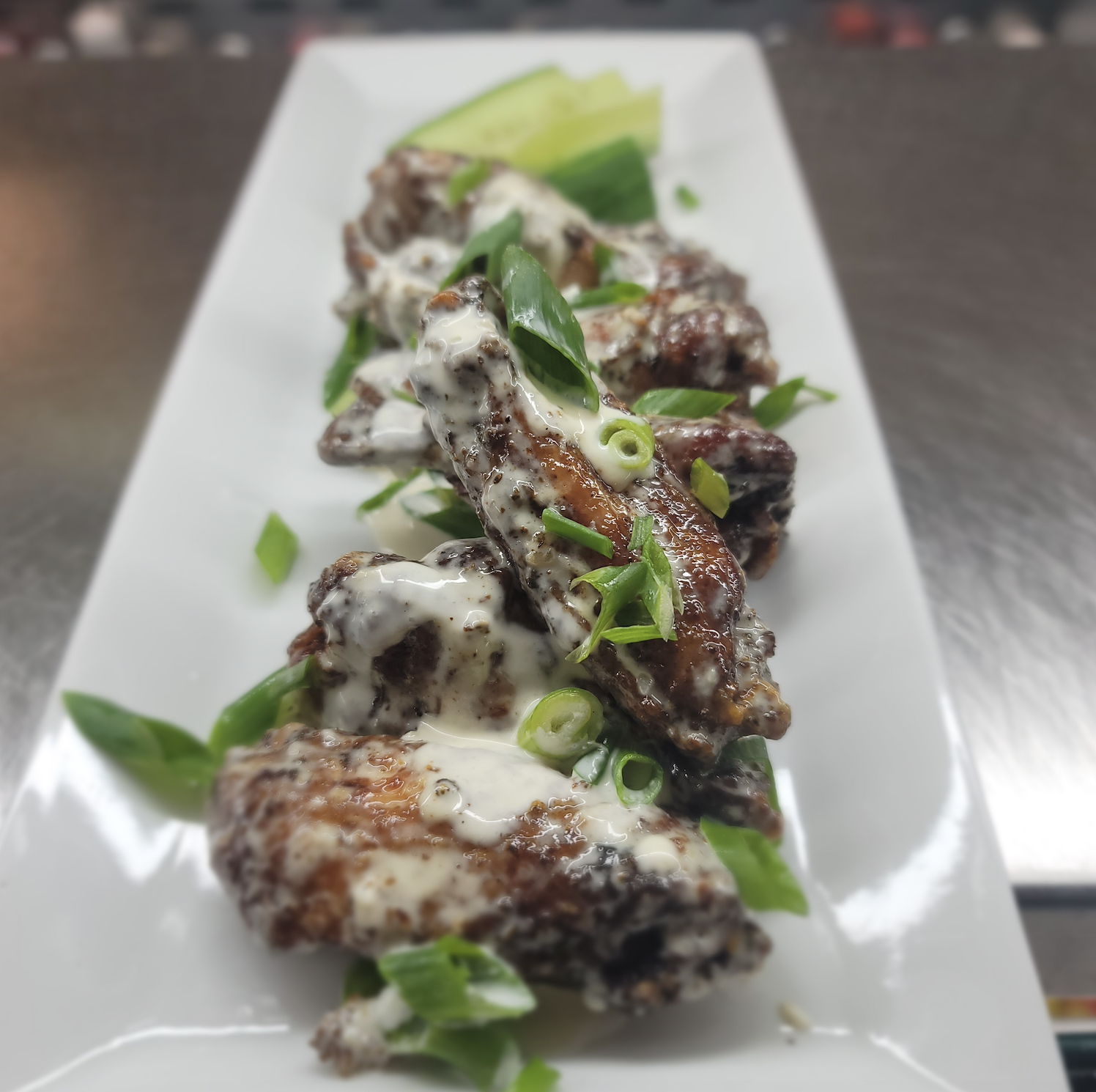 close up photo of a plate of wings with green onions on top 