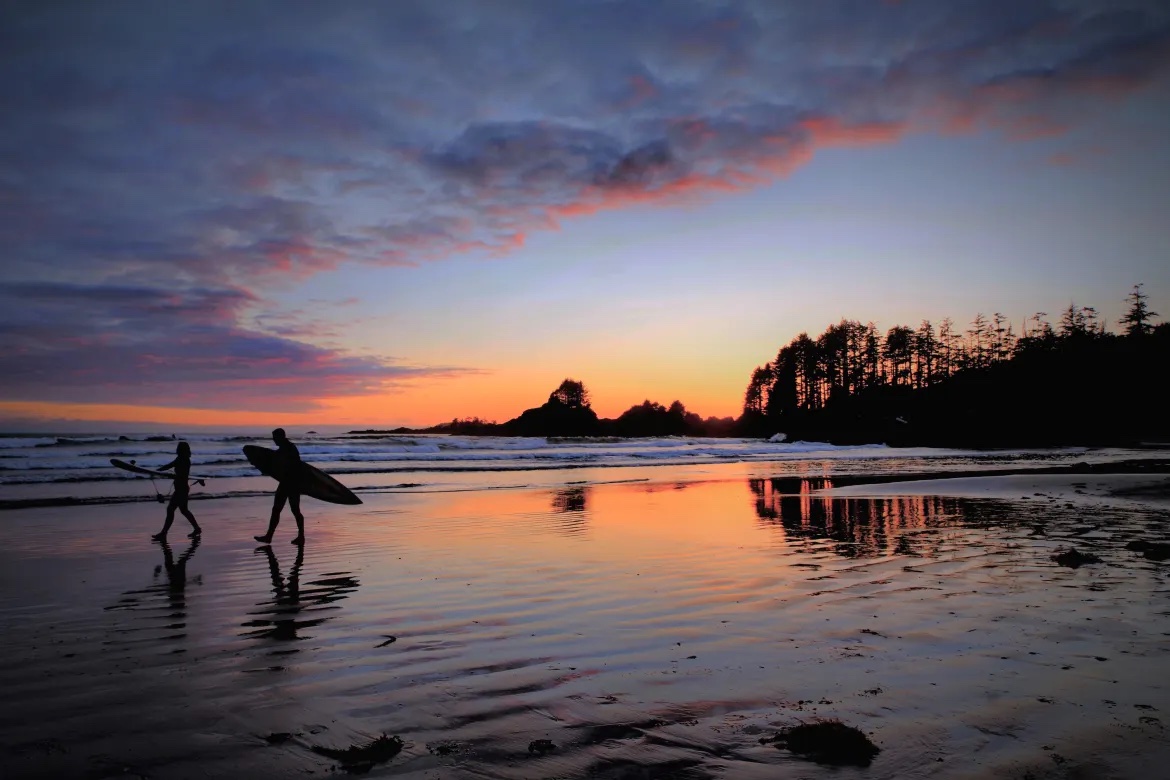 Cox Bay Beach at sunset with two surfers silhouetted against an orange sun