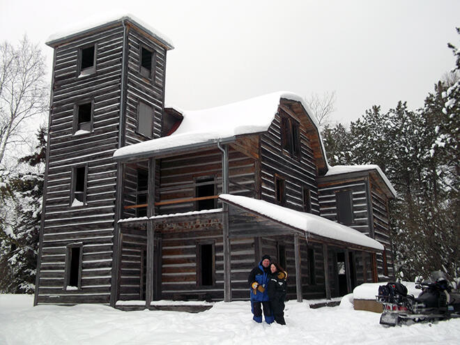 couple standing in front of abandoned wooden building in winter