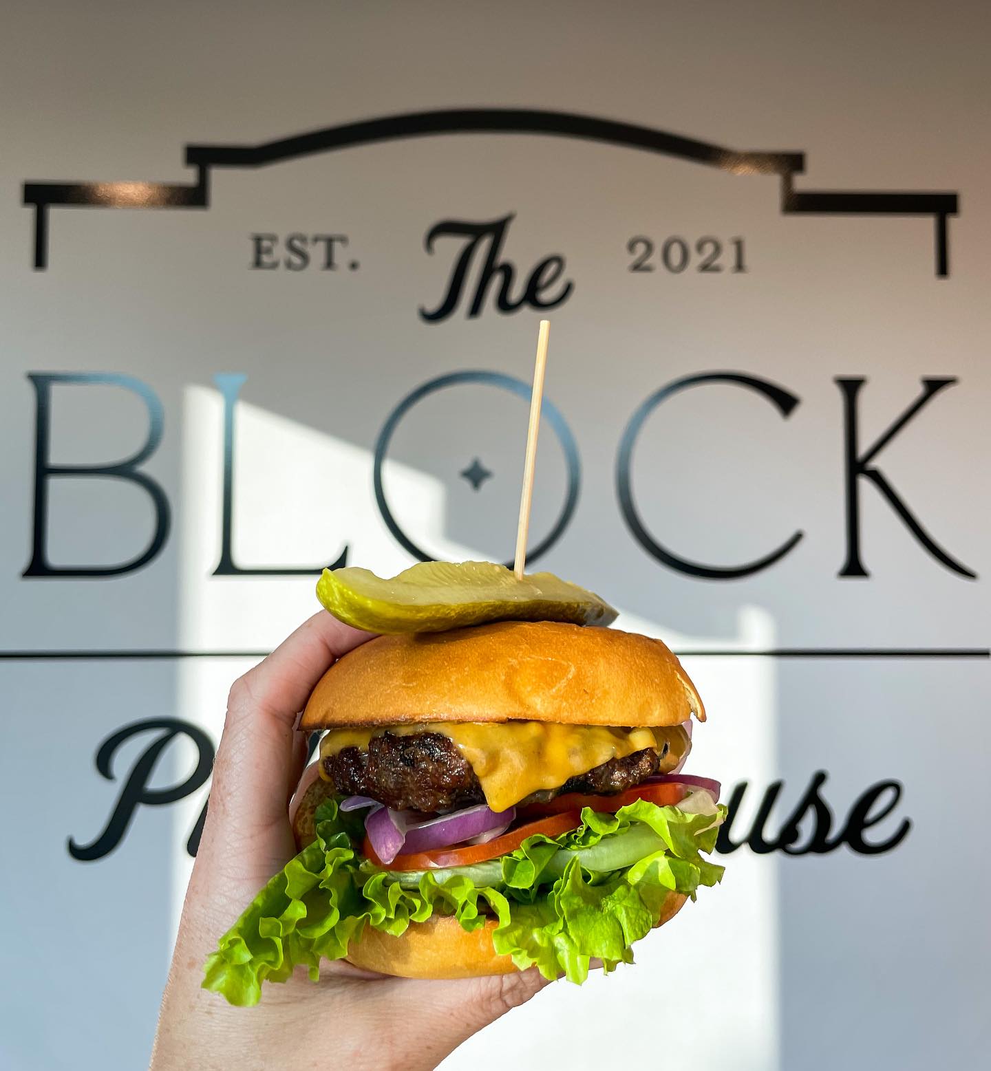 hamburger held up in front of The Block Public House sign