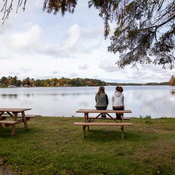 2 people sitting on picinc table overlooking a lake