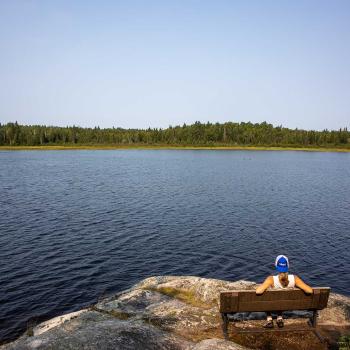 person sitting on bench over looking lake