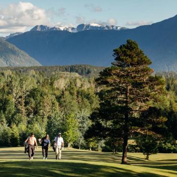 3 golfers walking the course with mountains in background