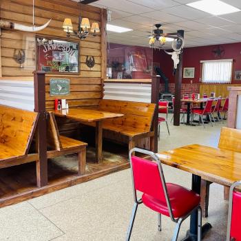 A restaurant dining room with wooden walls and tables, red chairs, and western decor