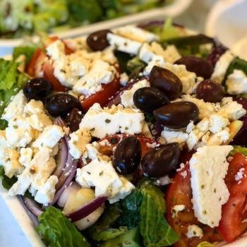 a close up of a bowl of salad with cheese and olives on top