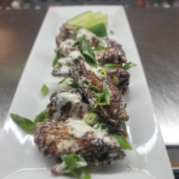 close up photo of a plate of wings with green onions on top 