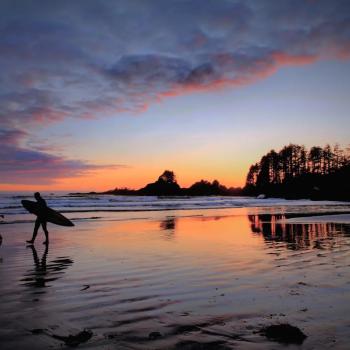 Cox Bay Beach at sunset with two surfers silhouetted against an orange sun