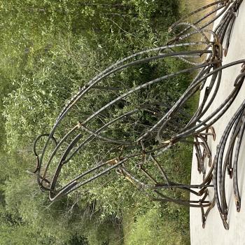 Metal sculpture of a toad with greenery in the background