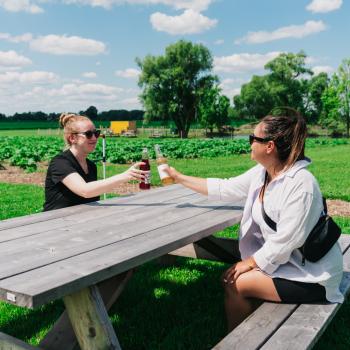 two people enjoying a drink on picnic table at Tall Post Craft Cider